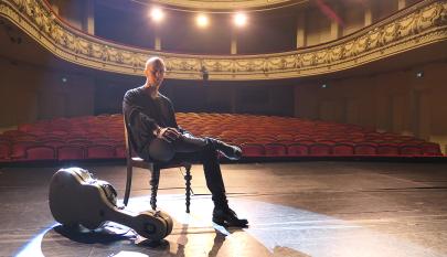 Joonas istuu tuolilla teatterin lavalla kitaralaukku vierellään